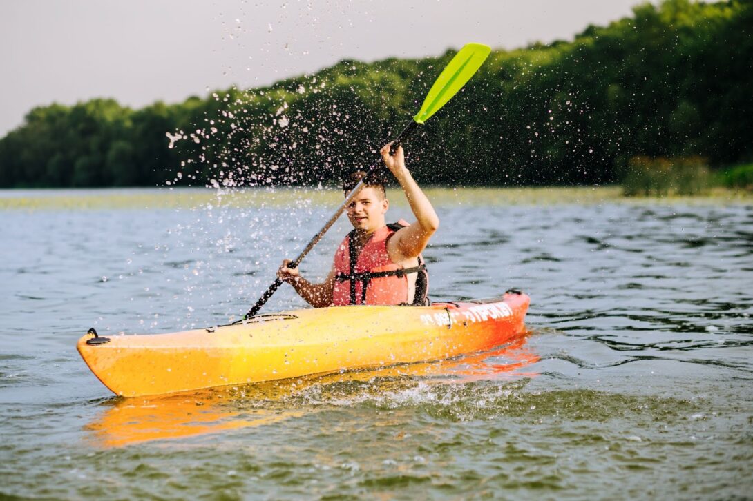 A person creating ripples in the water using a paddle while kayaking across a lake