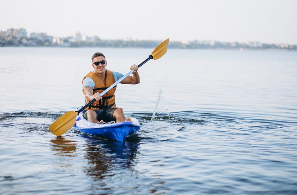 man kayaking on the river and holds a yellow canoe paddle