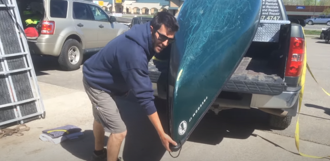 Man gripping canoe edge on pickup truck bed
