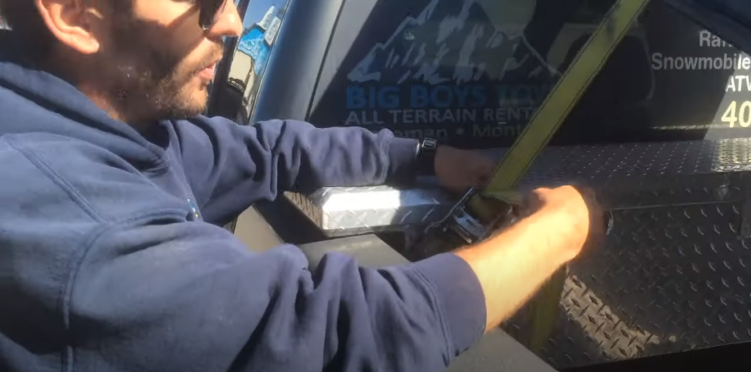Man fixing a strap on the back of a pickup truck