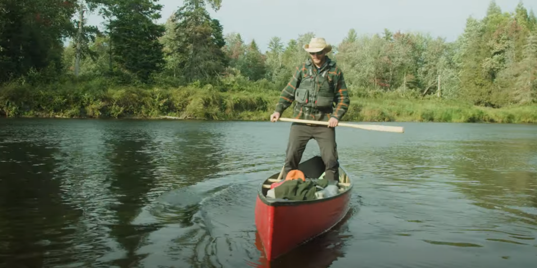 Man in hat holding paddle while standing on a canoe