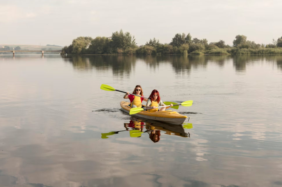two girls sitting with kayak on the river, trees on the background