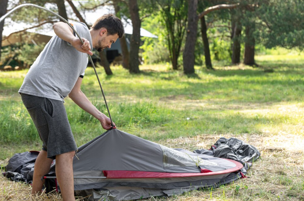 man setting up tent outdoors and trees behind