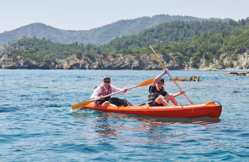 two people kayaking with paddles on the river and hills with trees behind