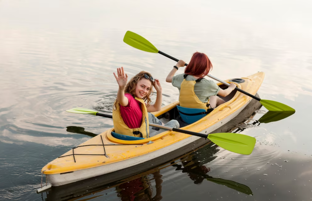 two woman kayaking with green paddles, one is smiling and waving her hand