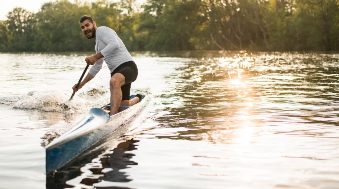 smiling man in kayak with a paddle on a river, trees behind him