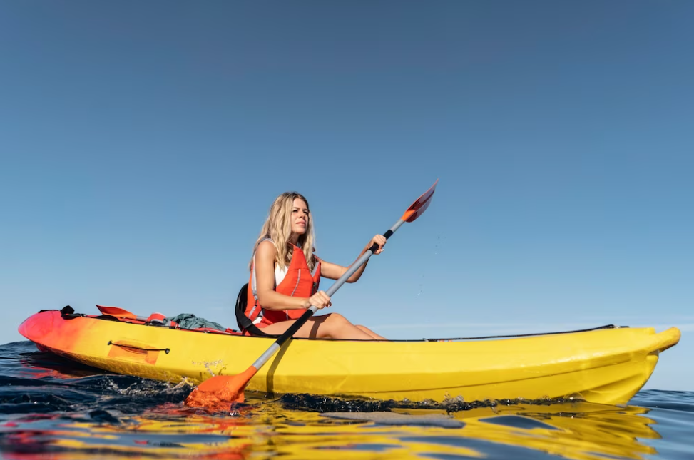 blonde woman sitting in a kayak and holding a yellow paddle on a river