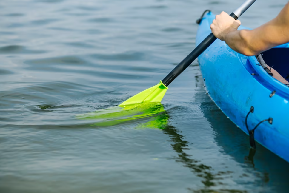 hand holding green paddle in a blue kayak on the river